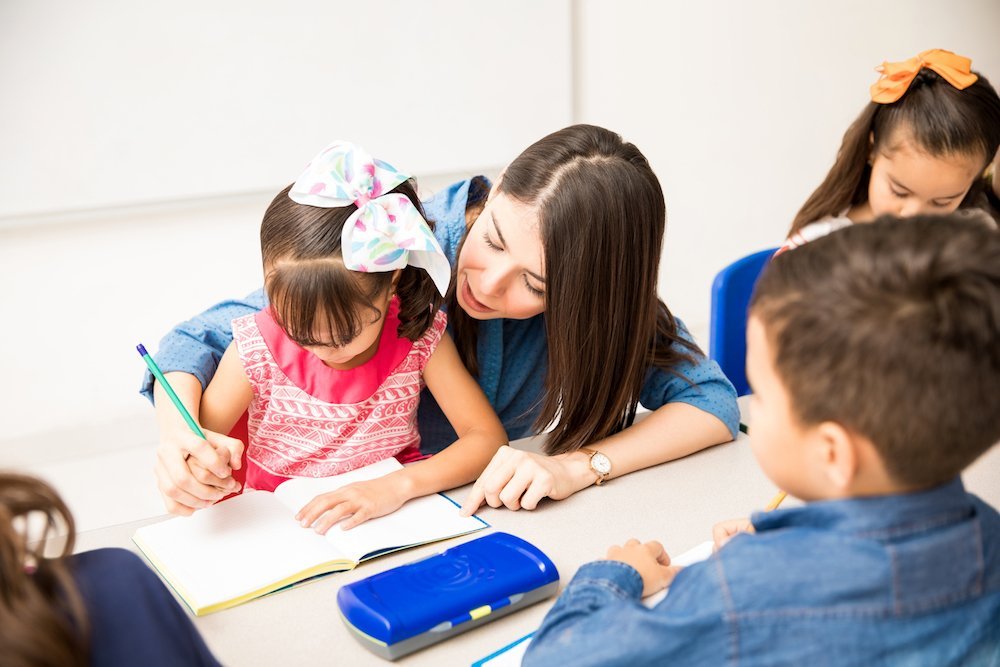 a teacher helping a little girl write in her book